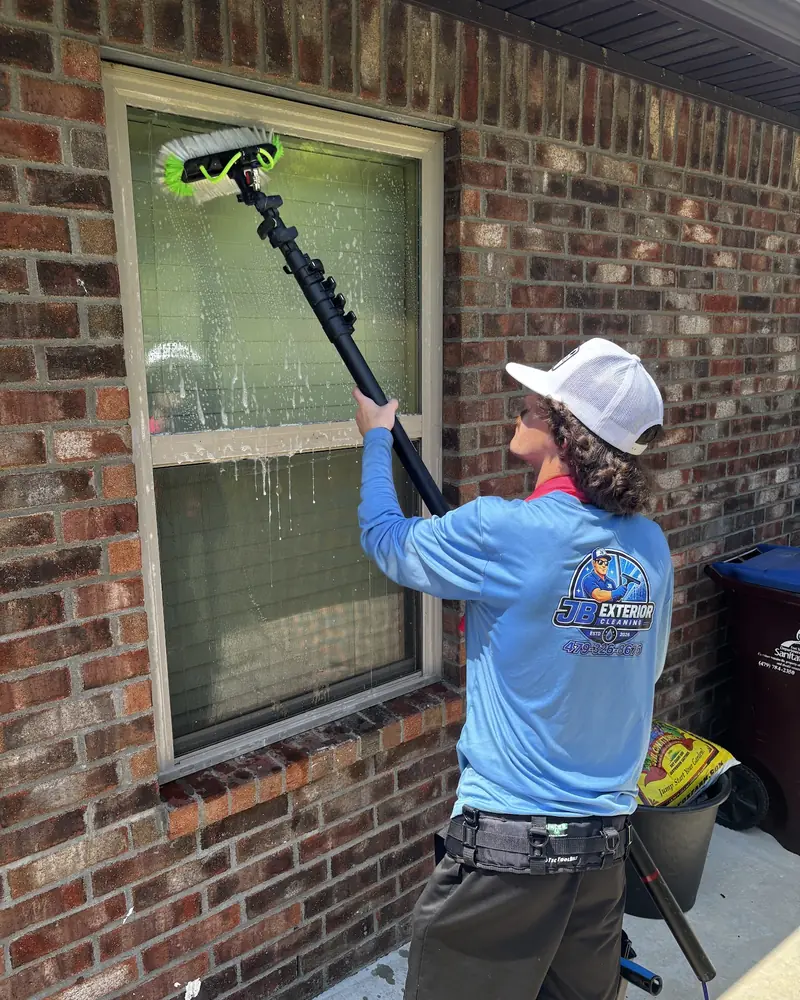 JB crew member cleaning a window on a brick home with a water-fed pole