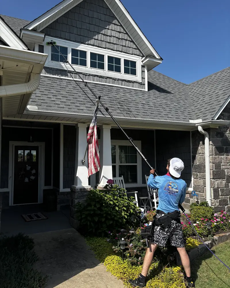 JB crew member cleaning windows on a stone-front home